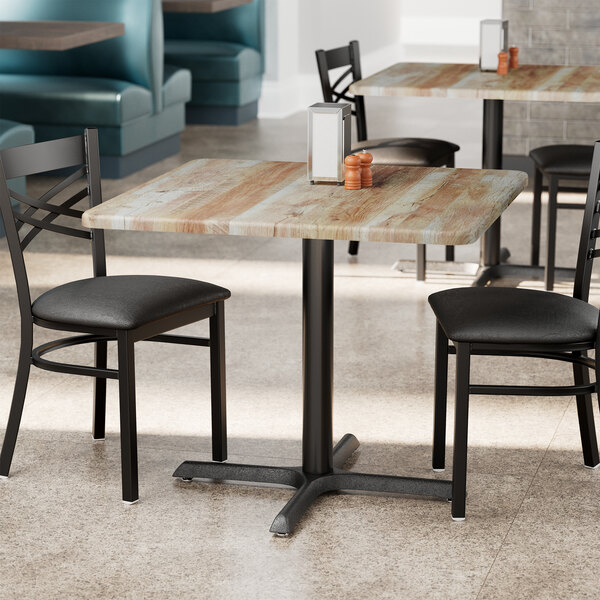 A Lancaster Table & Seating square table with a barnwood finish on it with chairs.