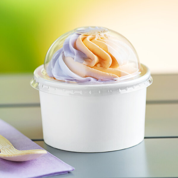 A white paper cup of frozen yogurt with a clear plastic dome lid.
