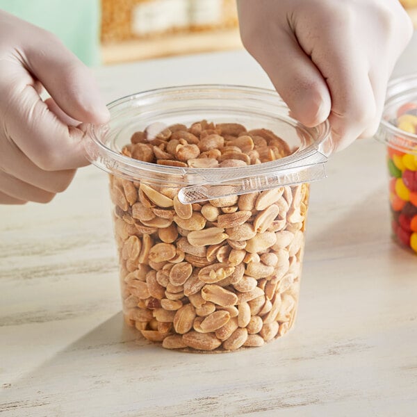 A hand holding an Inline Plastics round plastic container with peanuts.