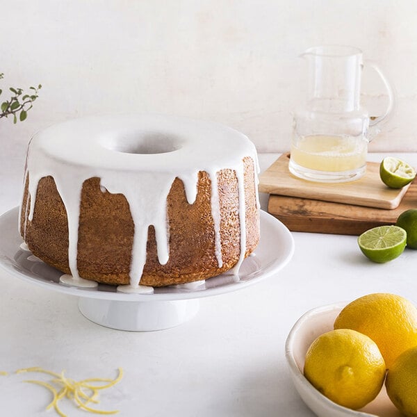 A Nordic Ware angel food cake with icing on top and lemons in a bowl.