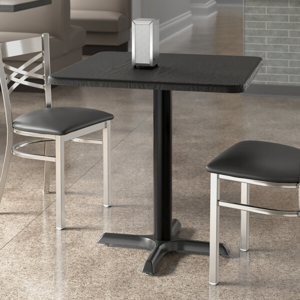 A black Lancaster Table & Seating square table top on a table with two chairs.