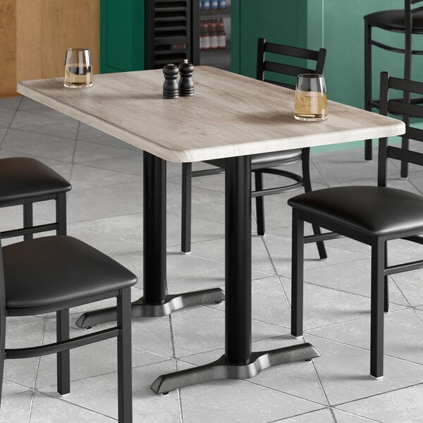 A rectangular standard height table with a gray wood finish and black metal legs, surrounded by black chairs.