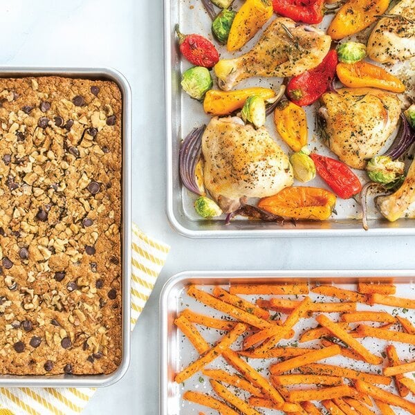 Three Nordic Ware aluminum sheet pans with baked sweet potatoes, carrots, and other vegetables.