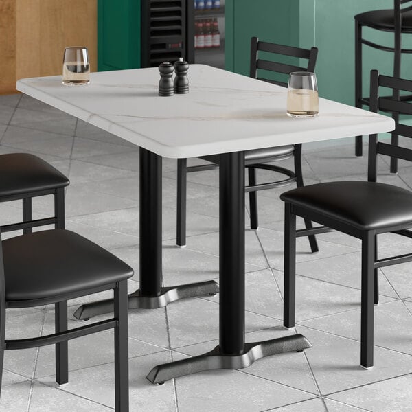 A white rectangular table with a white marble finish and black chairs.