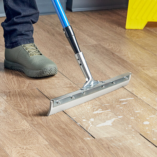 A person using a Lavex squeegee adapter on a mop to clean a wooden floor.