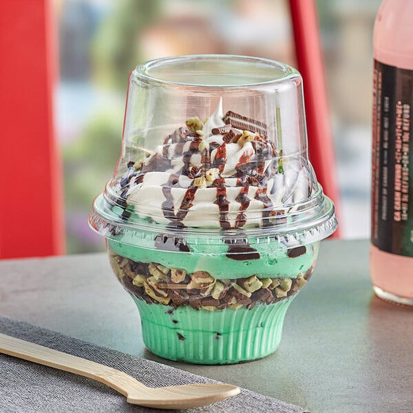 A clear plastic cup of ice cream with a tall dome lid and a wooden spoon.