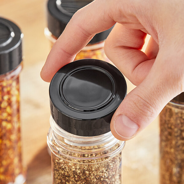 A hand holding a 48/485 black polypropylene cap on a jar of spices.