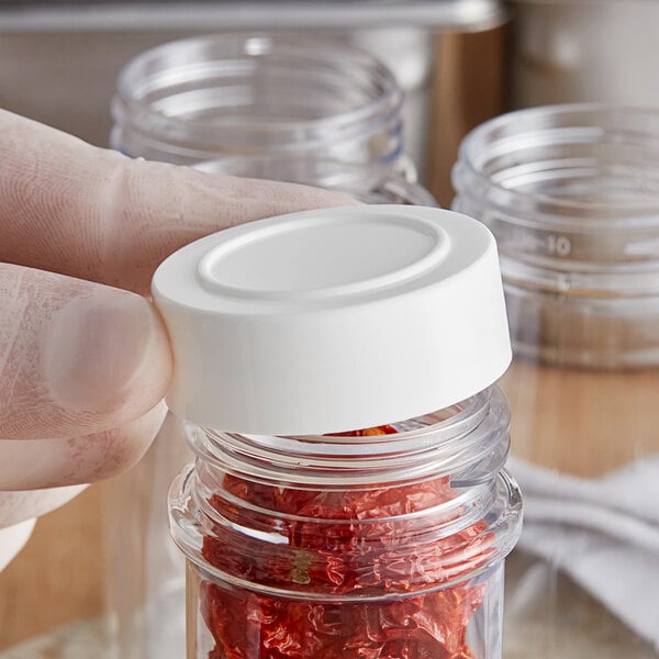 A hand holding a white jar of red peppers.