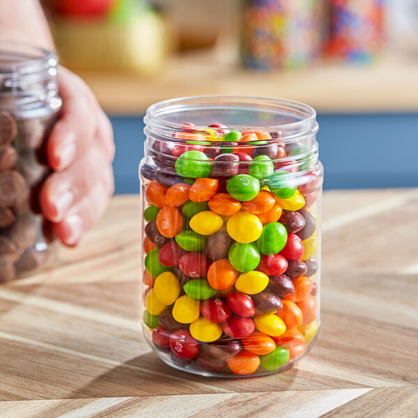 A person holding a clear round PET jar of candy.