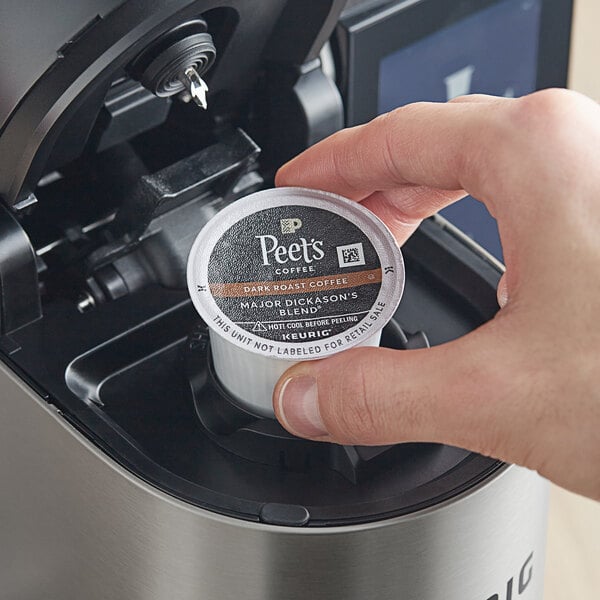 A hand holding a Peet's Coffee Major Dickason's Blend K-Cup pod over a Keurig machine.