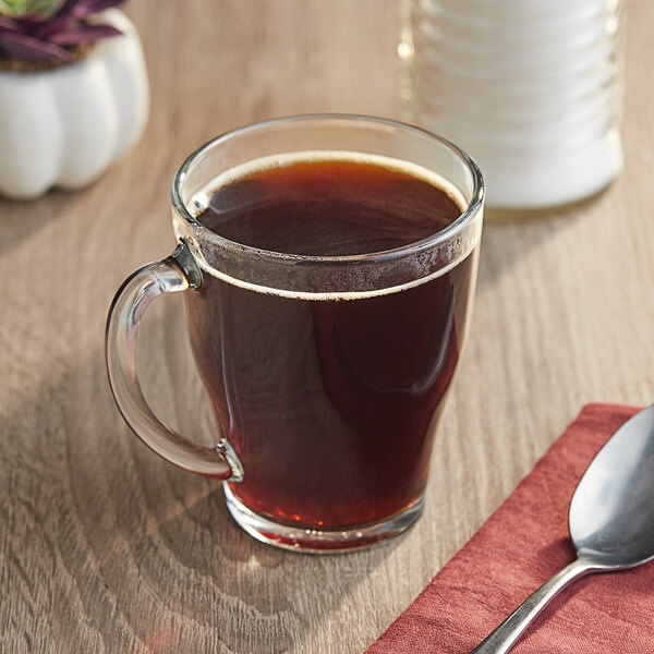 A glass mug of brown Peet's Coffee on a table with a spoon.