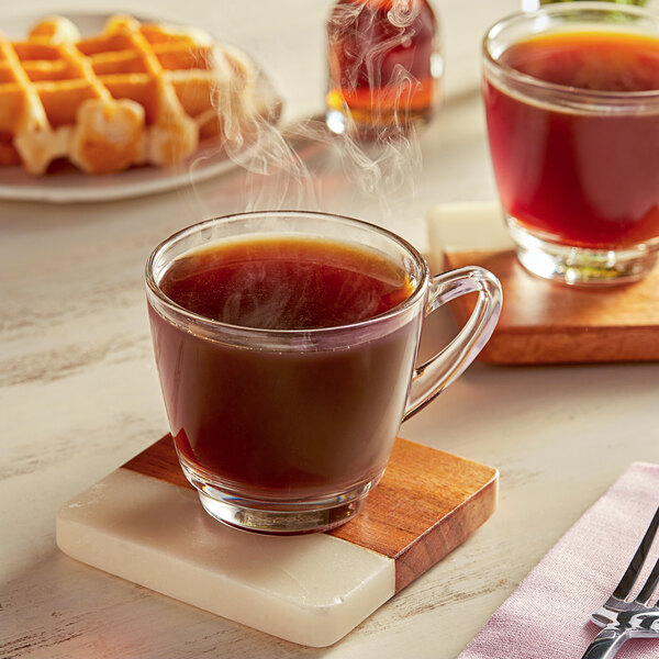 A wooden tray with a glass of illy Classico coffee on a coaster and a waffle.
