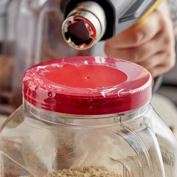 A person using a heat gun to shrink a clear band around a container with a red lid.