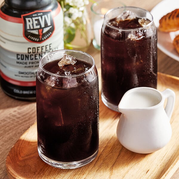 A glass of dark Revv Cold Brew coffee with ice and a bottle of coffee on a table.