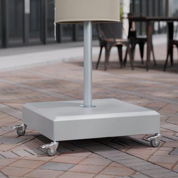 A Lancaster Table & Seating gray umbrella base on wheels under a table outdoors.