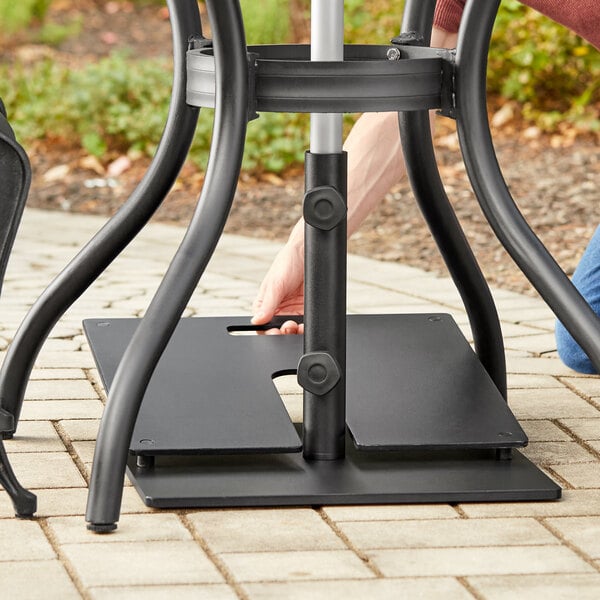 A person using a metal pole to adjust a Lancaster Table & Seating stack plate on a table outdoors.