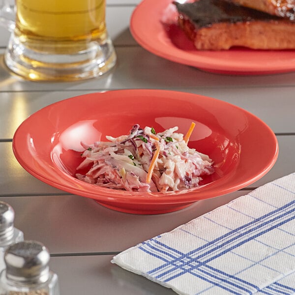 An Acopa Foundations orange melamine bowl of coleslaw on a table with a plate of food and a glass of beer.