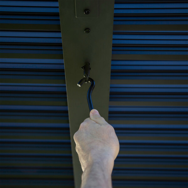 A hand holding a black metal hook over a gray aluminum louvered roof.