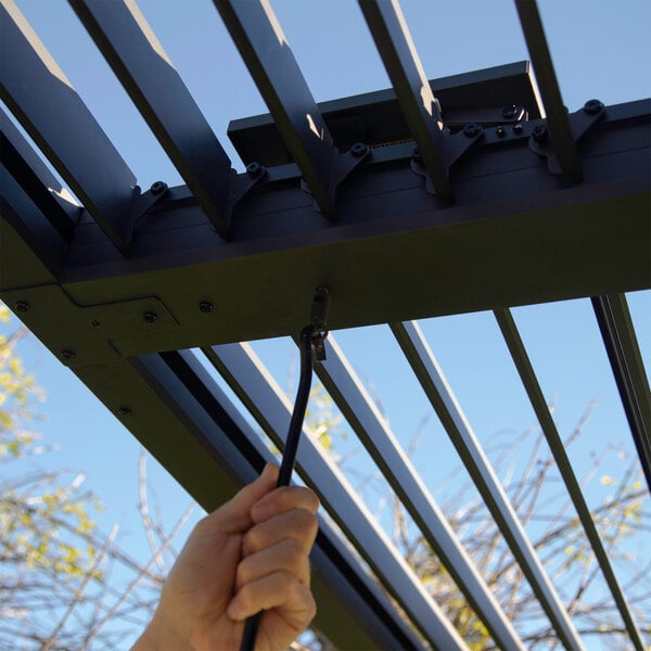 A person using a black cord to adjust the metal louvers on a Paragon Outdoor aluminum pergola.