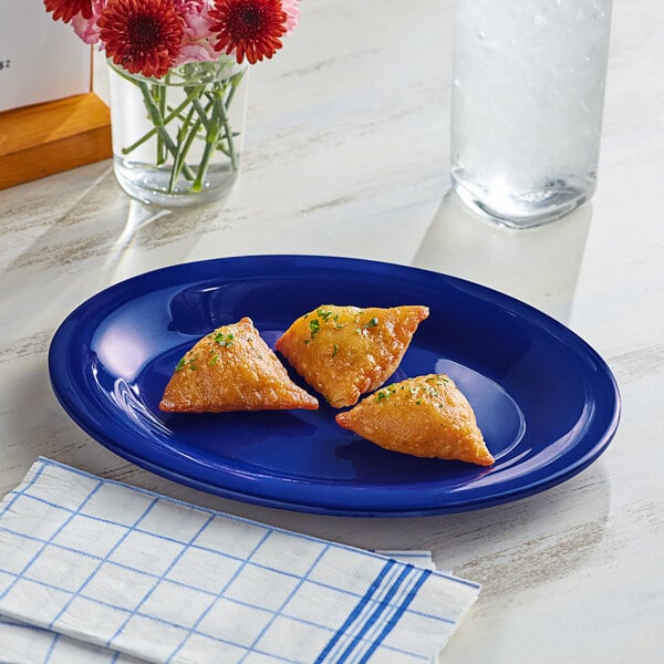 A blue Acopa Foundations melamine platter with food on it next to a glass of water and flowers.