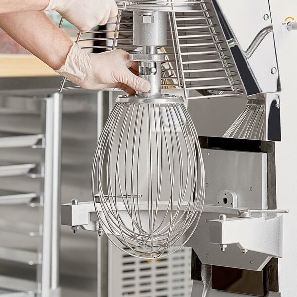 A person wearing gloves uses a Main Street Equipment wire whip to mix dough with a Galaxy mixer.