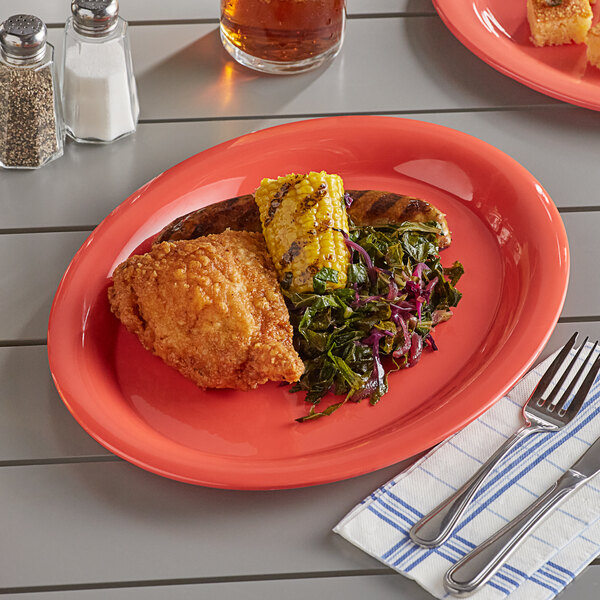 An Acopa Foundations orange wide rim melamine platter with food on a table with a fork and knife.