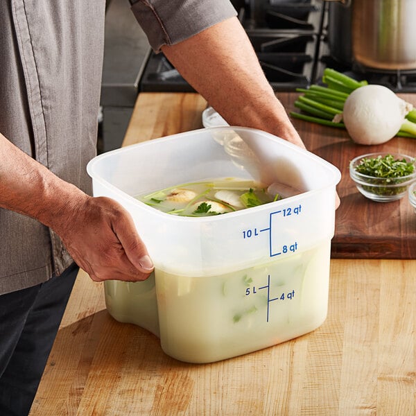 A man holding a Cambro translucent square food storage container of soup.