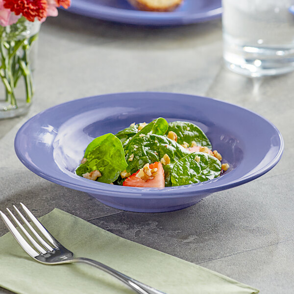 A bowl of spinach salad with a fork on a table set with a glass of water.