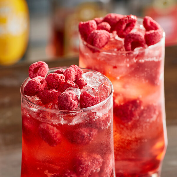 Two glasses of red raspberry cocktails garnished with raspberries.