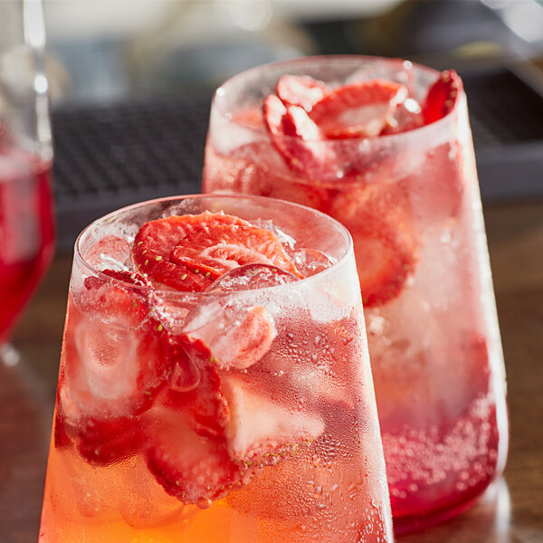 Two glasses of red strawberry drinks with ice and garnish, each garnished with freeze-dried strawberry slices.