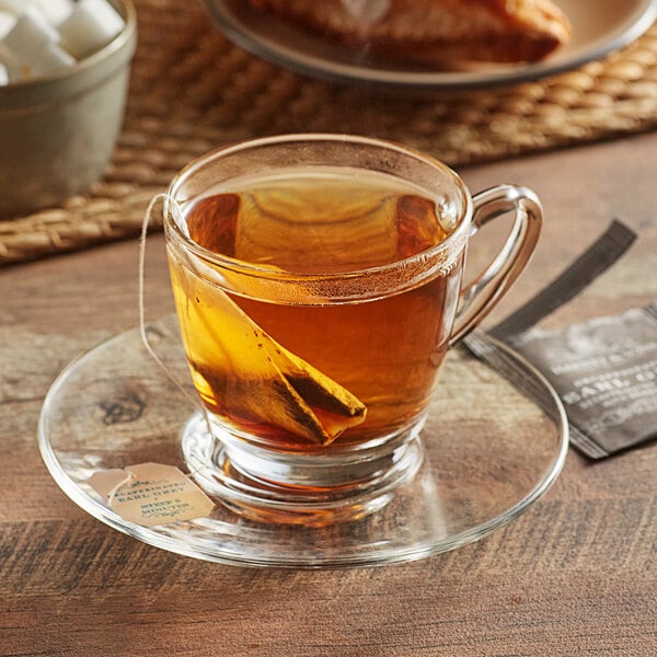 A glass cup of Harney & Sons decaf Earl Grey tea on a saucer with a tea bag in it.