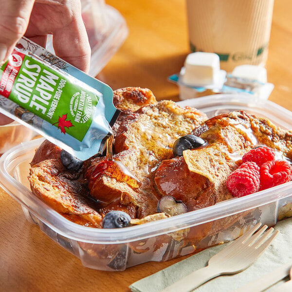 A hand pouring Butternut Mountain Farm maple syrup from a packet onto french toast.