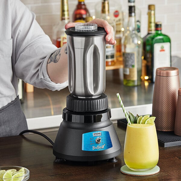 A person using a Waring BevBasix commercial bar blender to make a yellow drink.