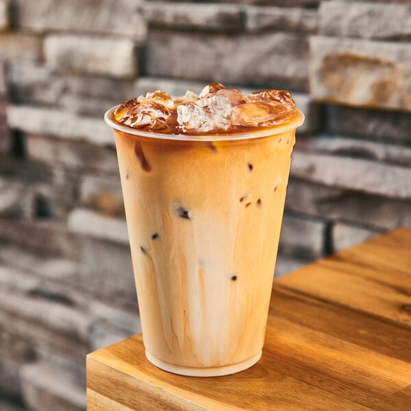 A Tossware Natural plastic cup of iced coffee on a wood table.
