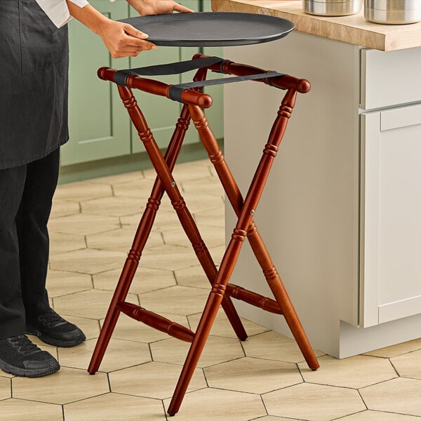 A person holding a tray on a Lancaster Table & Seating mahogany wood folding tray stand.