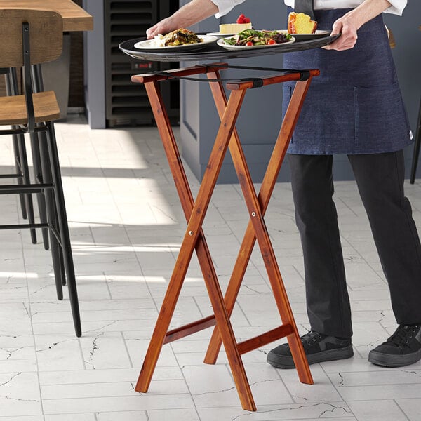 A person holding a Lancaster Table & Seating walnut wood folding tray stand with food on it.