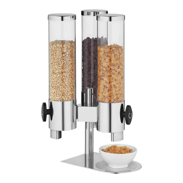 A Hepp by Bauscher stainless steel and glass cereal dispenser filled with cereal next to a bowl of cereal.