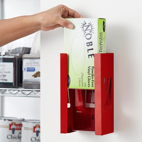 A person holding a box of gloves in a red dispenser.