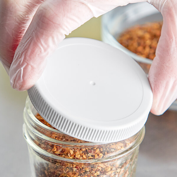 A person in gloves holding a jar of food with a white ribbed plastic cap.
