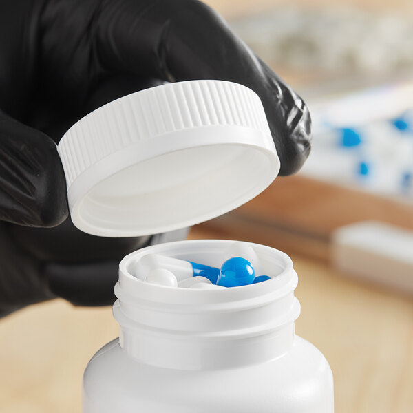 A hand in a black glove opening a white bottle of blue pills with a white plastic cap.