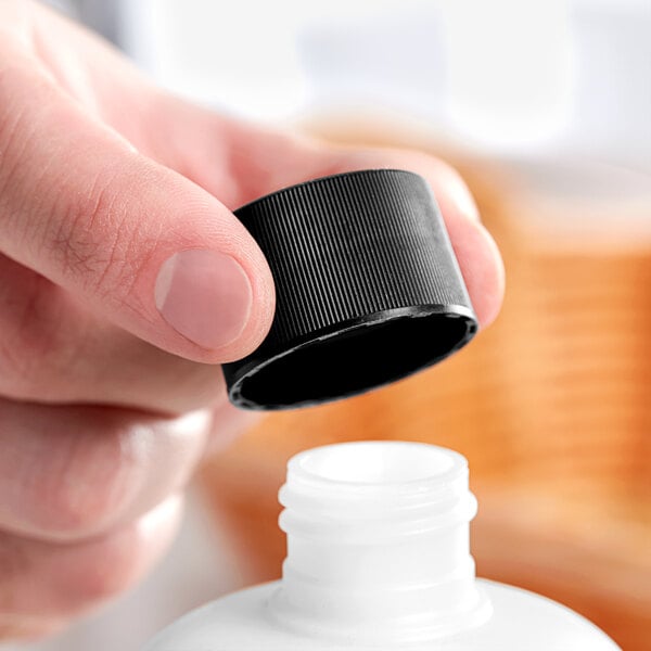 A hand holding a 28/410 black plastic bottle cap over a white bottle.