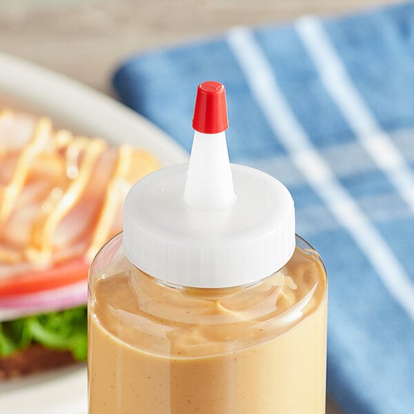 A bottle of mustard with a white 38/400 natural Yorker spout cap on a table in a deli.