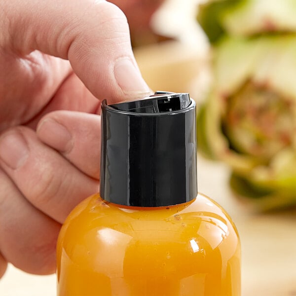 A person using a 28/410 black unlined disc top lid on a bottle of orange liquid.