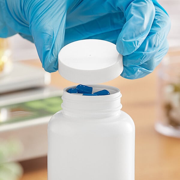 A hand in blue gloves holding a white plastic cap over a white bottle.