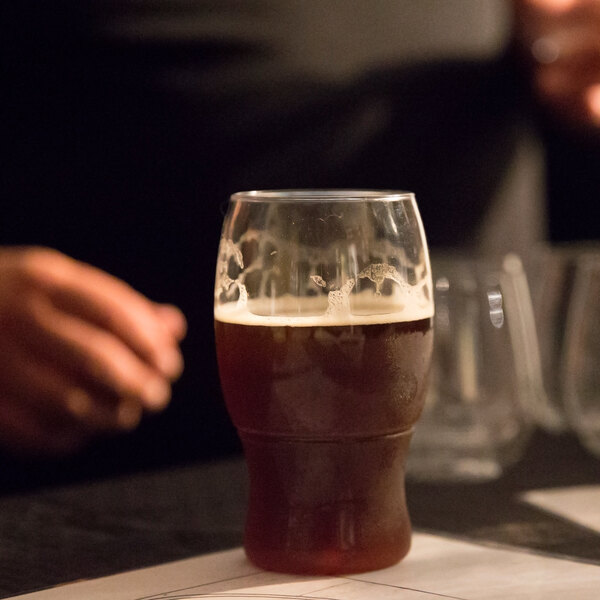 A Tossware POP plastic pint glass filled with dark liquid on a table in a bar.