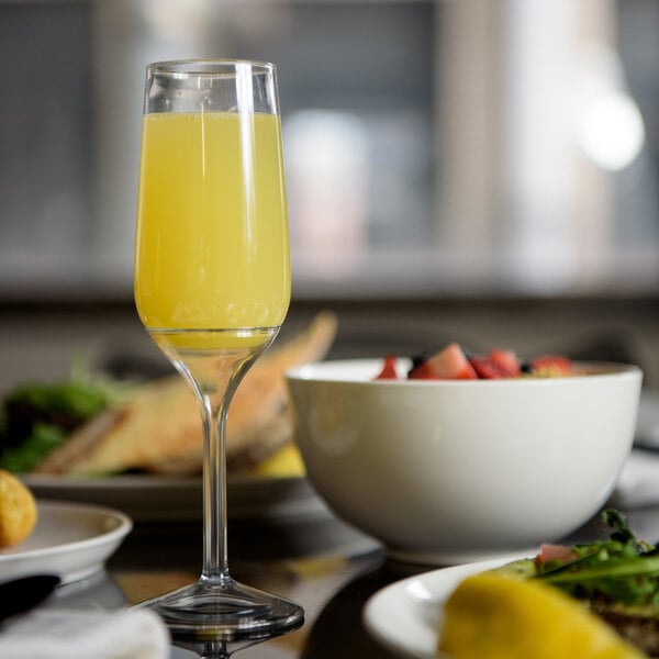 A Tossware small stem glass of orange juice on a table next to a bowl of food.