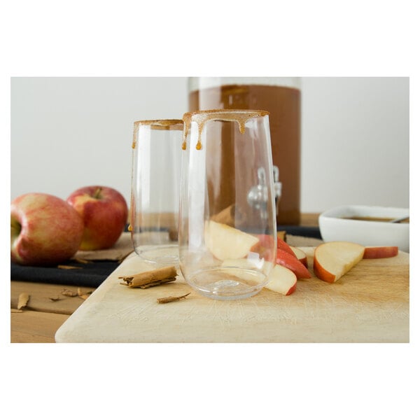 Two Tossware plastic champagne flutes filled with apple cider and garnished with a slice of apple.