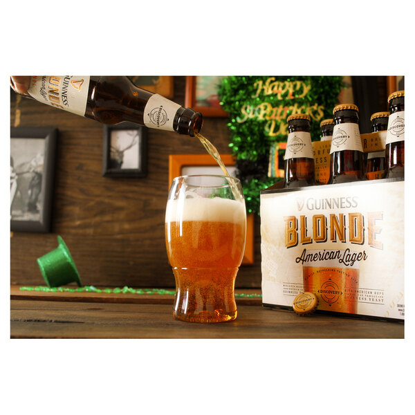 A person pouring a bottle of beer into a Tossware plastic pint glass.