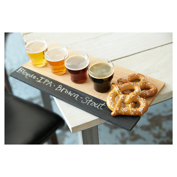 A Tossware plastic taster glass of beer on a tray with pretzels.