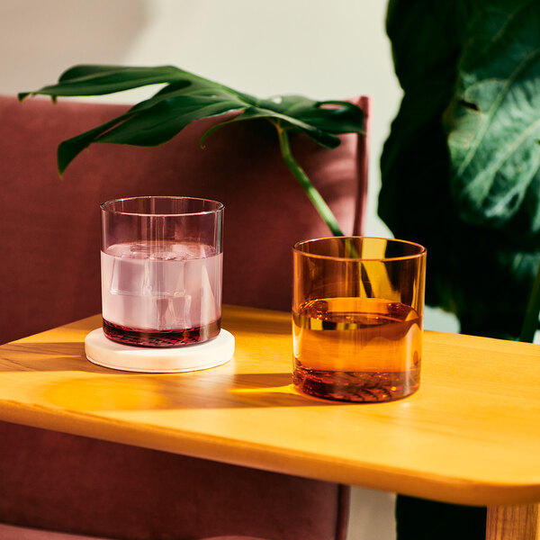 Two Tossware amber plastic rocks glasses filled with liquid on a table.